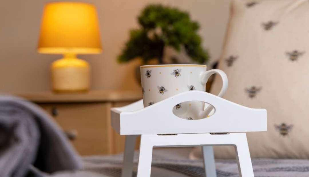 Breakfast tray with mug on bed, cosy scene with lamp and plants