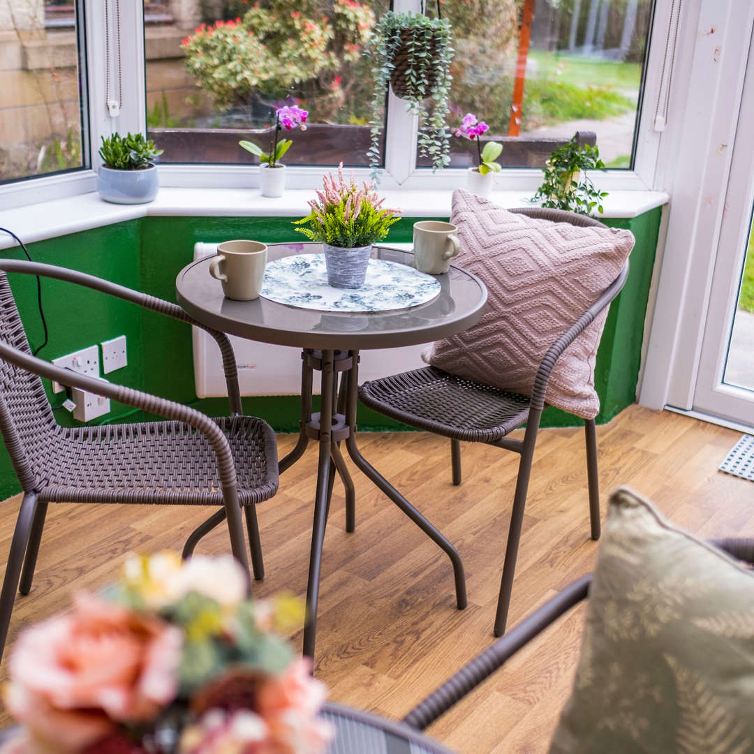 Rattan furniture sits within a bright and airy conservatory which is adorned with plants and colourful decor