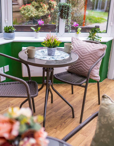 Rattan furniture sits within a bright and airy conservatory which is adorned with plants and colourful decor