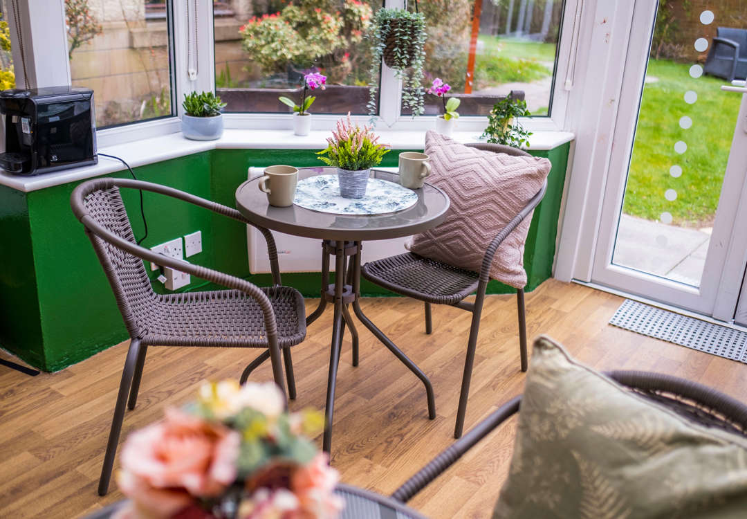 Rattan furniture sits within a bright and airy conservatory which is adorned with plants and colourful decor