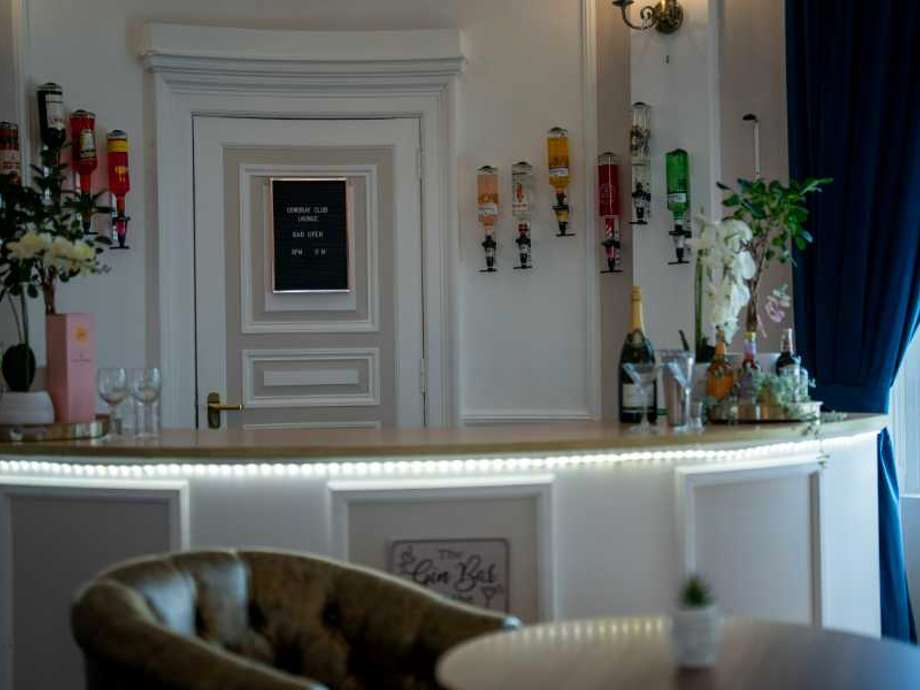 Elegant white bar showcasing a variety of liquors and glassware. Bottles adorn the wall, complemented by decorative glasses and flowers