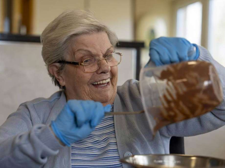 A care home resident smiles as she pours melted chocolate into a large bowl for baking