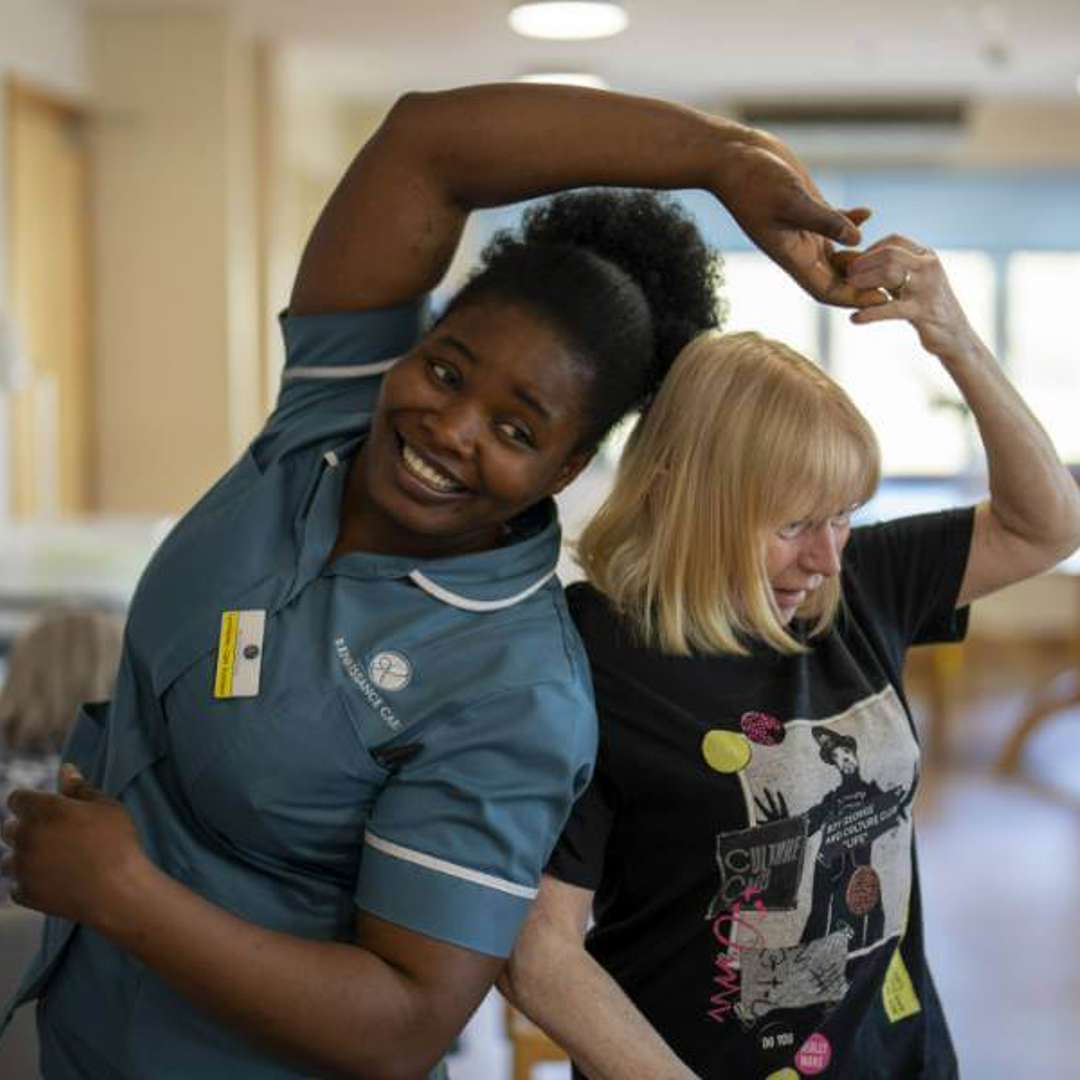 Staff member and resident dance together in a communal lounge