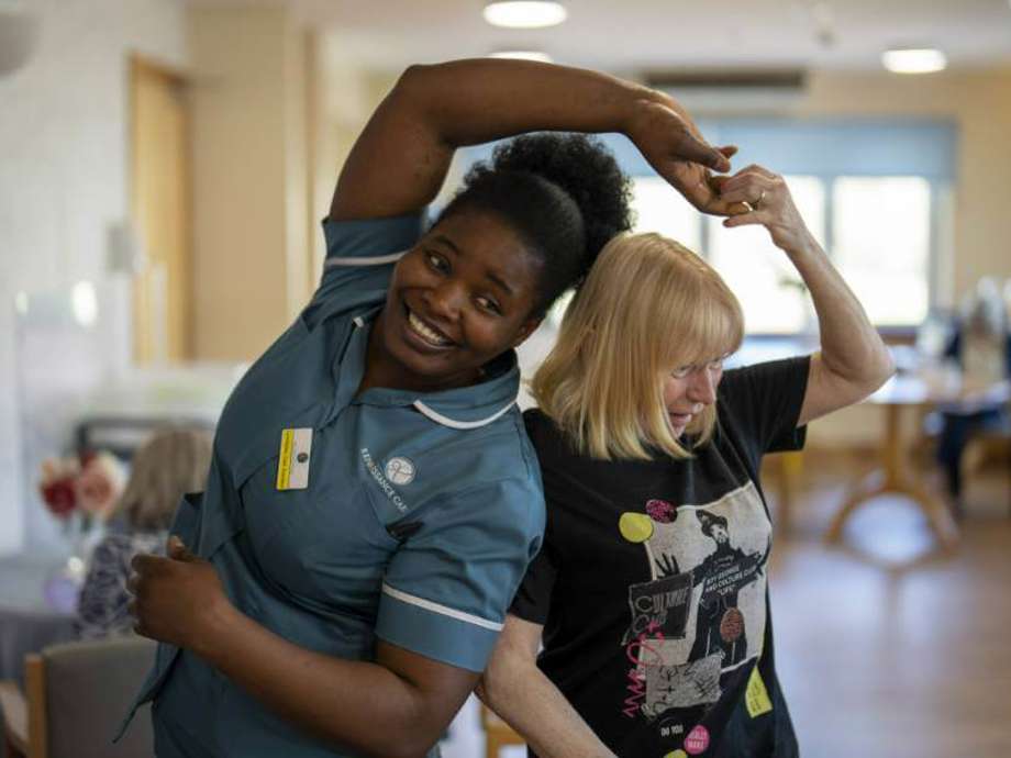 Staff member and resident dance together in a communal lounge