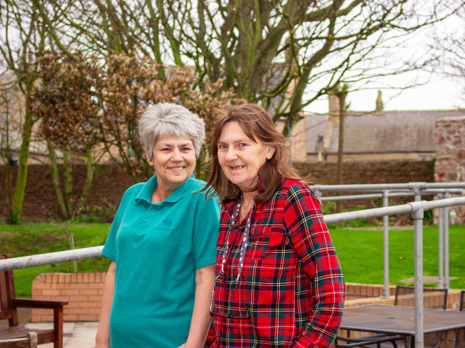 A care home resident and staff member enjoy a walk together in the care home garden.