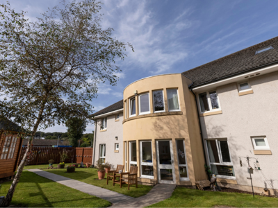 Exterior view of Jesmond Care Home with white and cream painted walls. A summer house is visible on the left side.