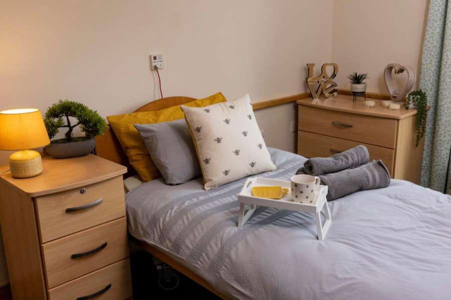 Wooden bedroom furniture with a bed in grey and yellow linens. Soft lighting, plants, and bee decorations