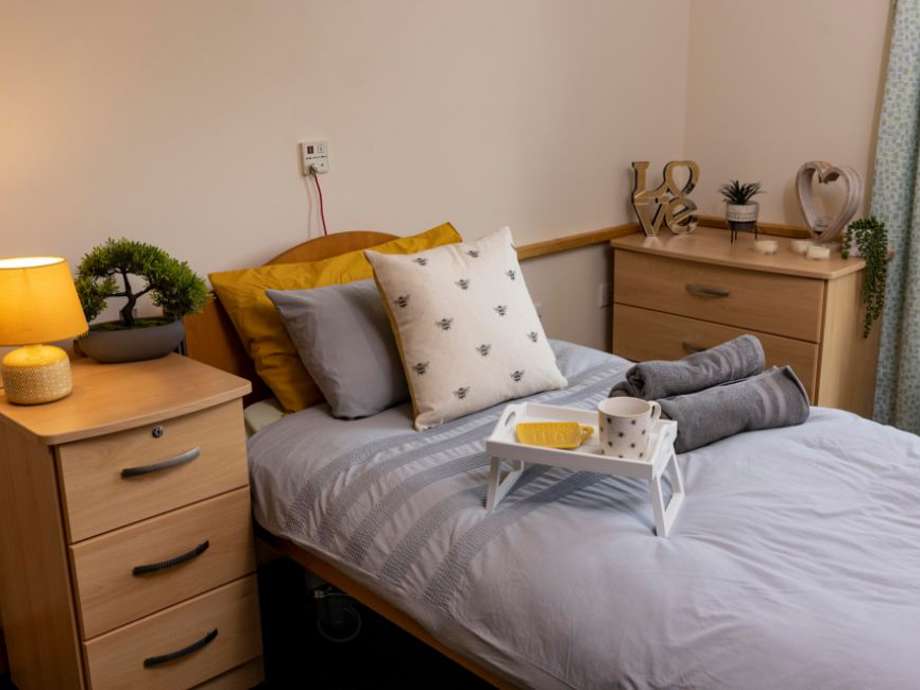 Wooden bedroom furniture with a bed in grey and yellow linens. Soft lighting, plants, and bee decorations