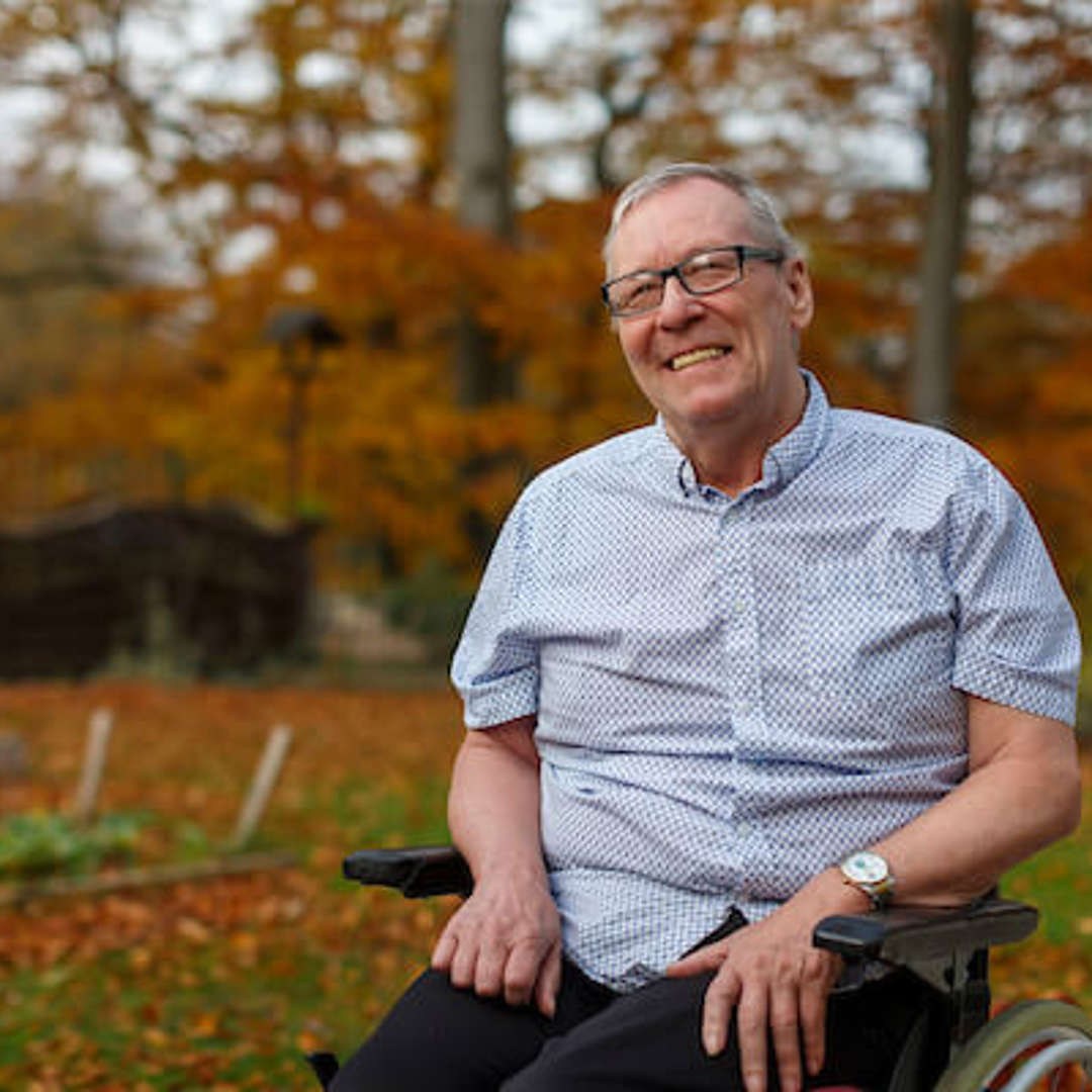 A care home resident smiles, he is enjoying time in the Autumnal garden