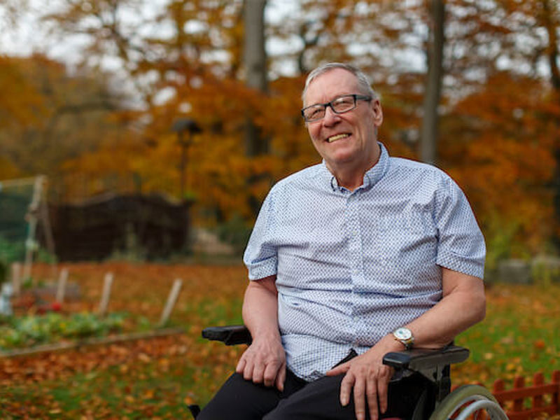 A care home resident smiles, he is enjoying time in the Autumnal garden
