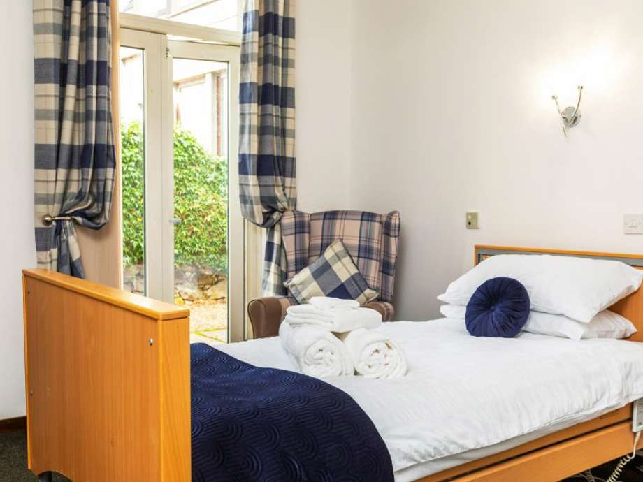 Care home bedroom in a modern white and navy color scheme. Wooden furniture complements the spacious feel created by large patio doors.