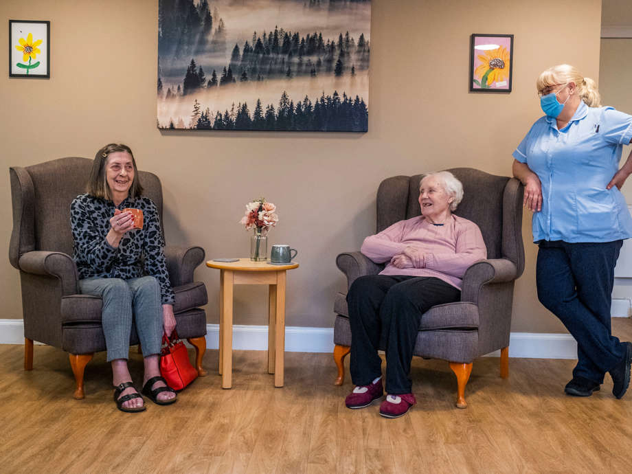 Residents enjoy tea in the common area, supported by a friendly staff member