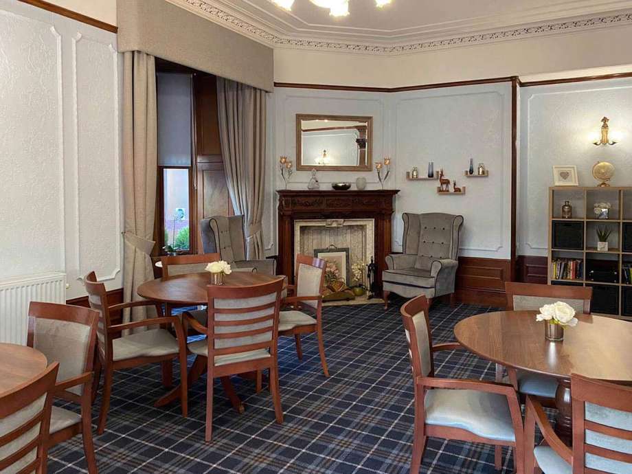 A spacious lounge in a period property, featuring a fireplace as the central focal point, surrounded by tables and chairs.