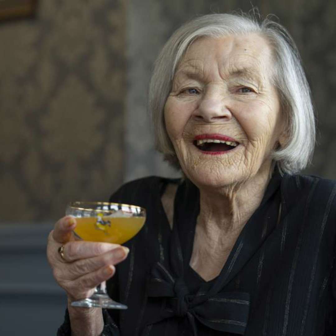 A care home resident smiles brightly, holding up a colourful cocktail 