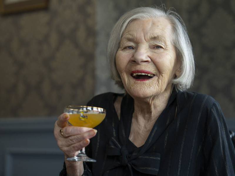 A care home resident smiles brightly, holding up a colourful cocktail 