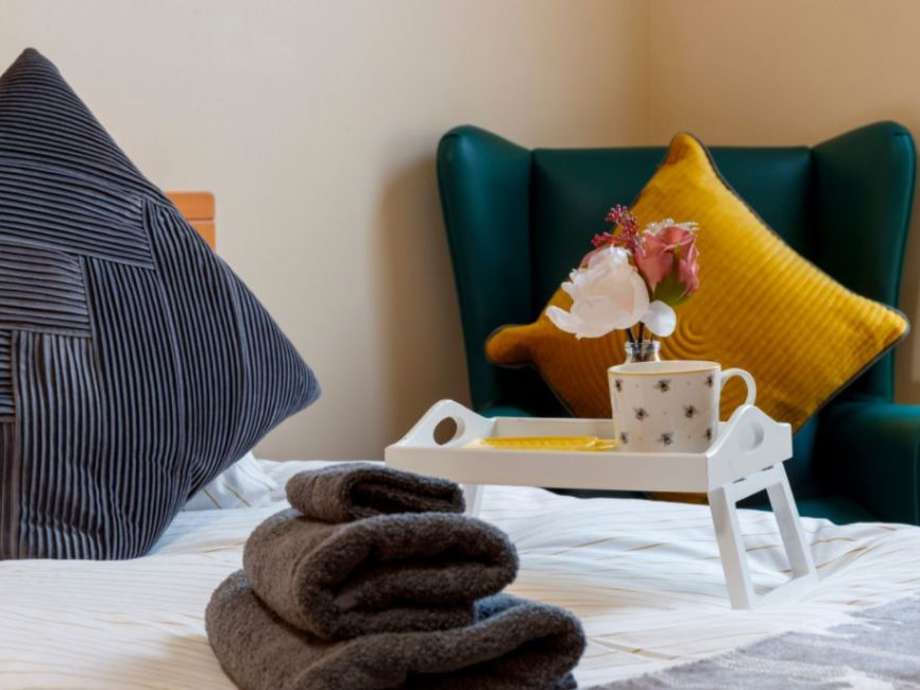 A bedroom set up with a white duvet, fluffy towels, a breakfast tray, and armchair