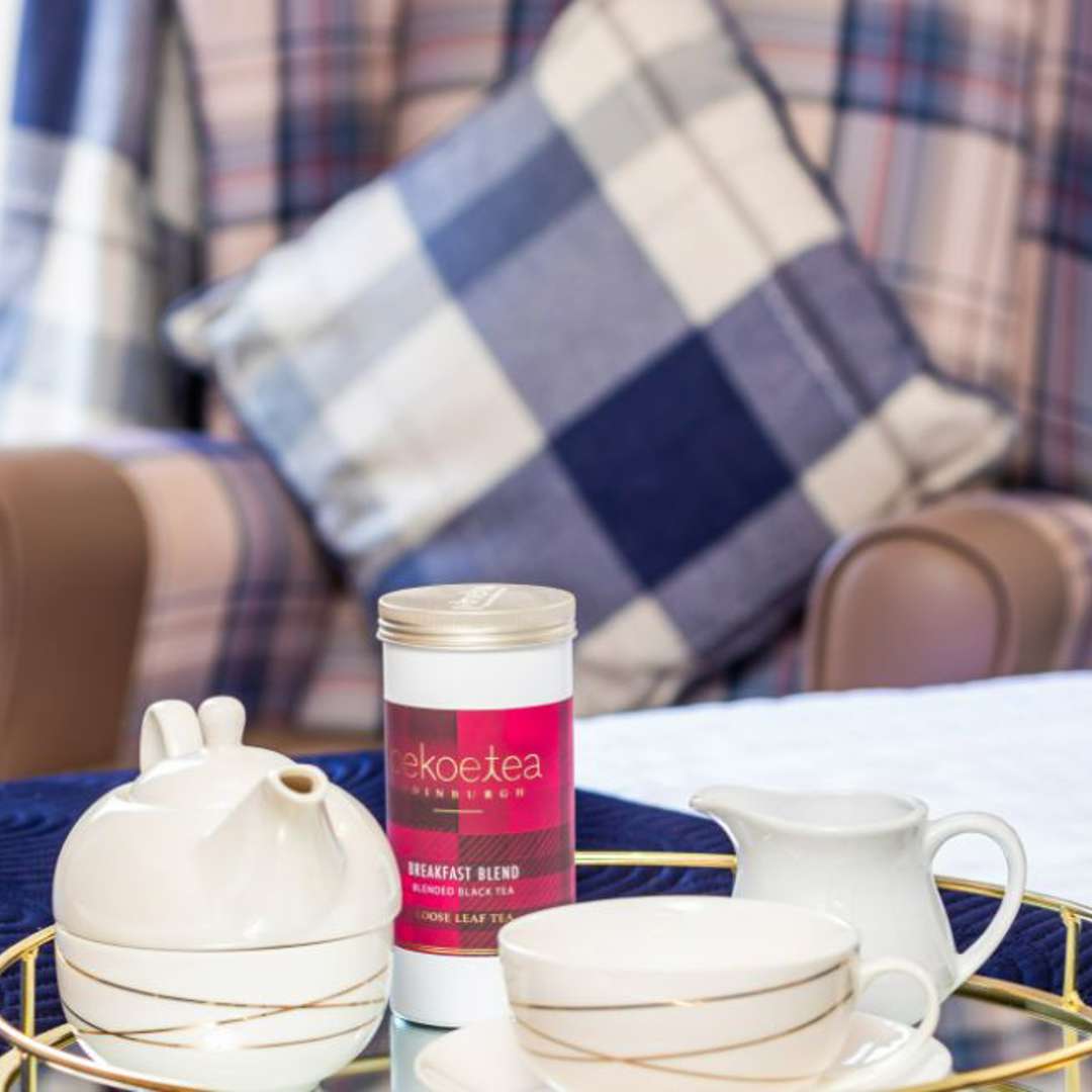 Cosy teatime treat. Tea set with Pukka tea on a tray rests on a bed. A navy tartan chair adds a touch of comfort