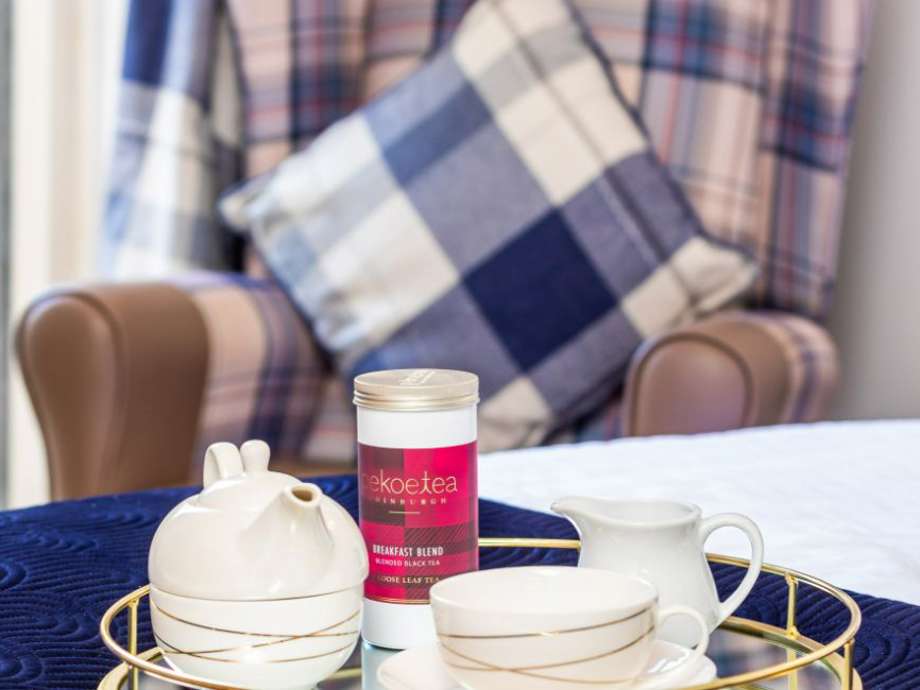 Cosy teatime treat. Tea set with Pukka tea on a tray rests on a bed. A navy tartan chair adds a touch of comfort