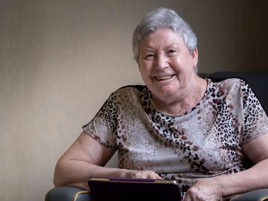 A woman, sitting on a grey chair and smiling, using a tablet 