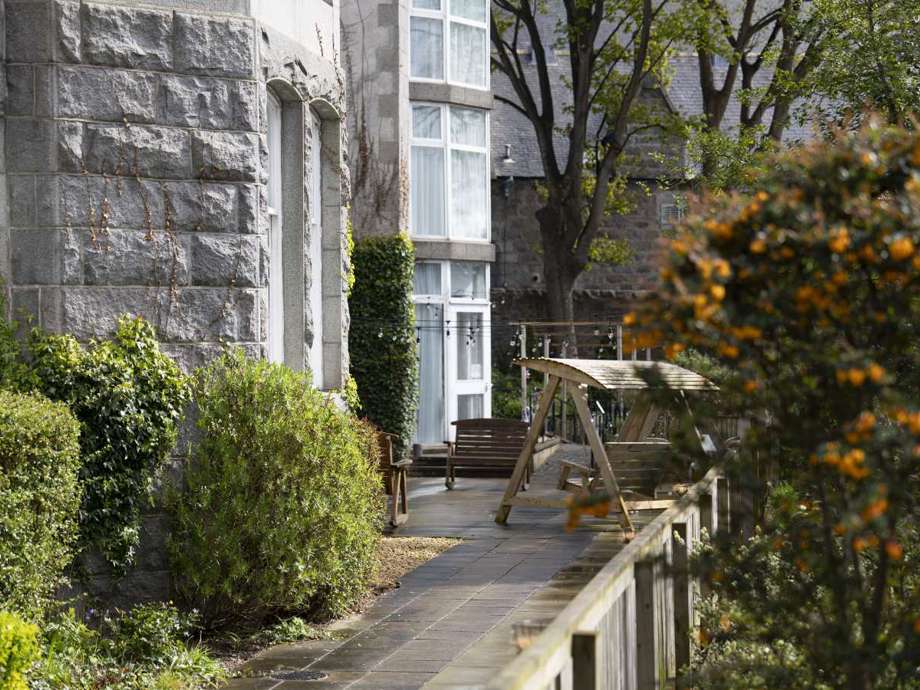 Serene care home garden featuring a relaxing patio with comfortable seating. Lush greenery surrounds the space, creating a tranquil atmosphere.