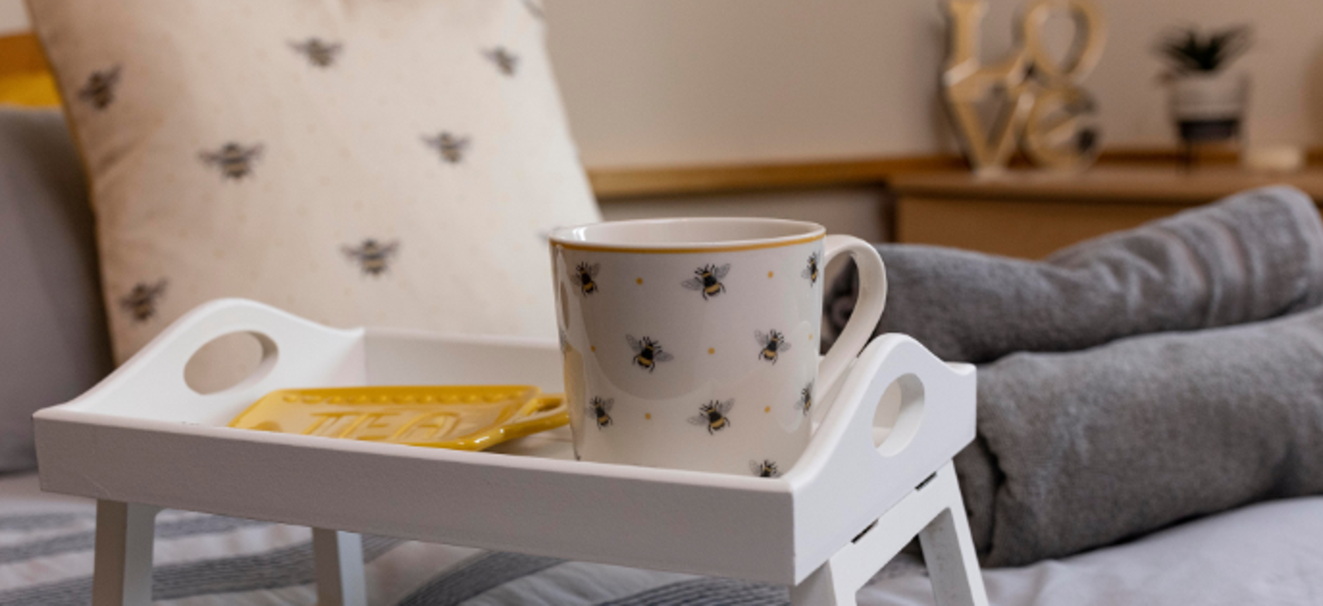 A breakfast tray sits atop a bed, with cosy features and bee detailing. 