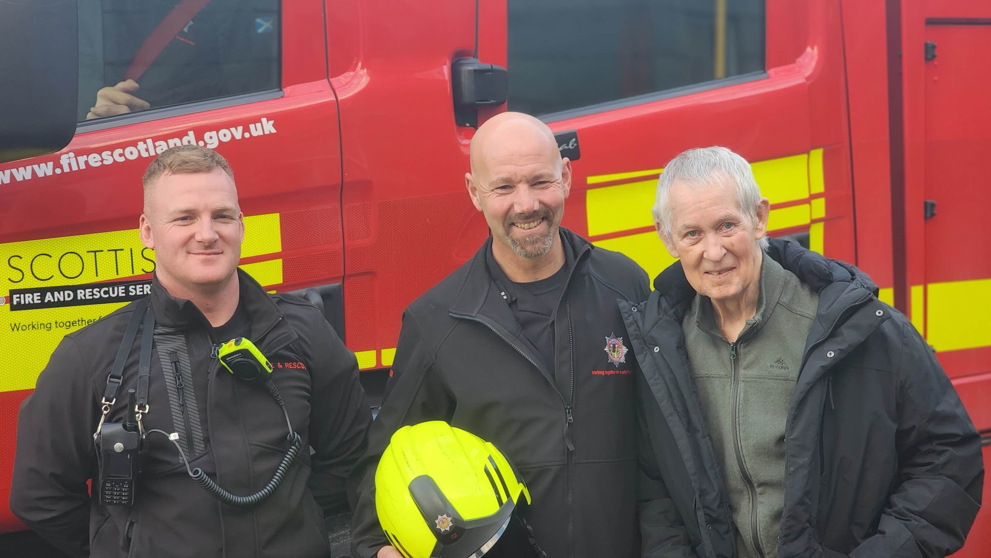 two firemen smile proudly holding a fire helmet as they stand next to ex-fireman Billy