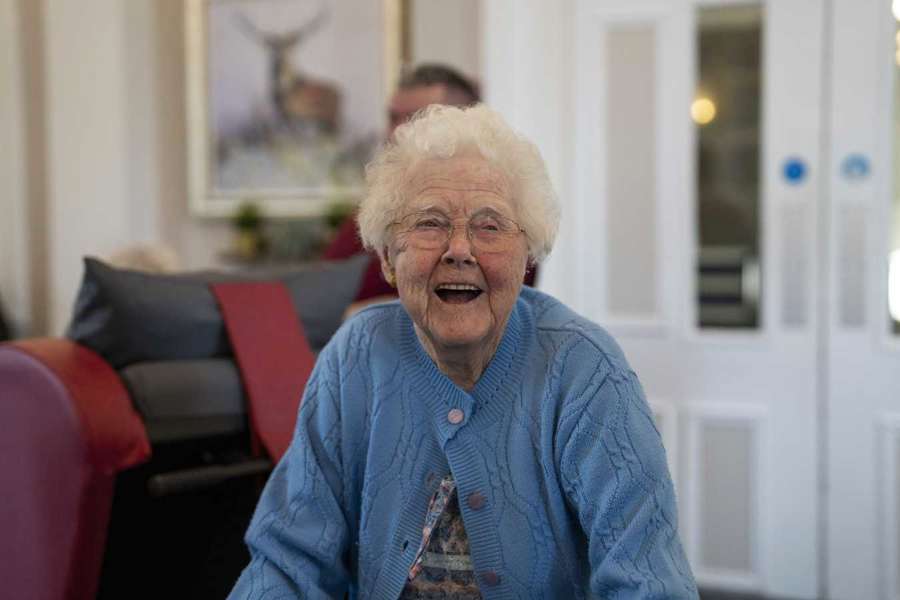 A woman in blue laughs while walking through a communal lounge