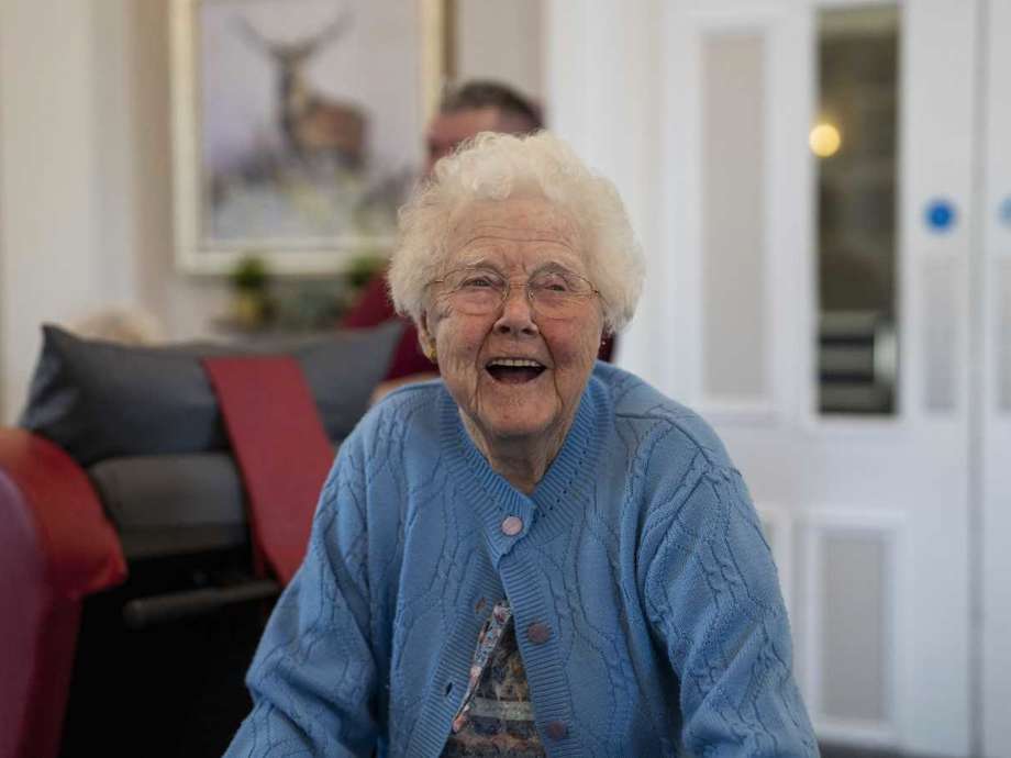 A woman in blue laughs while walking through a communal lounge