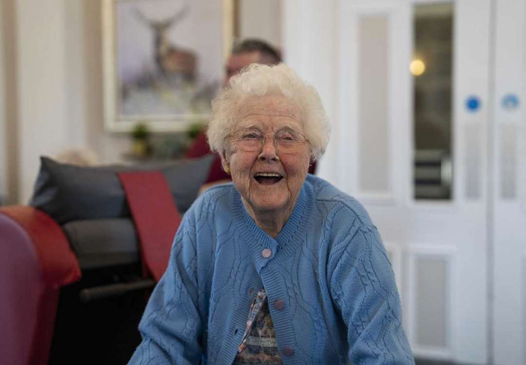 A woman in blue laughs while walking through a communal lounge