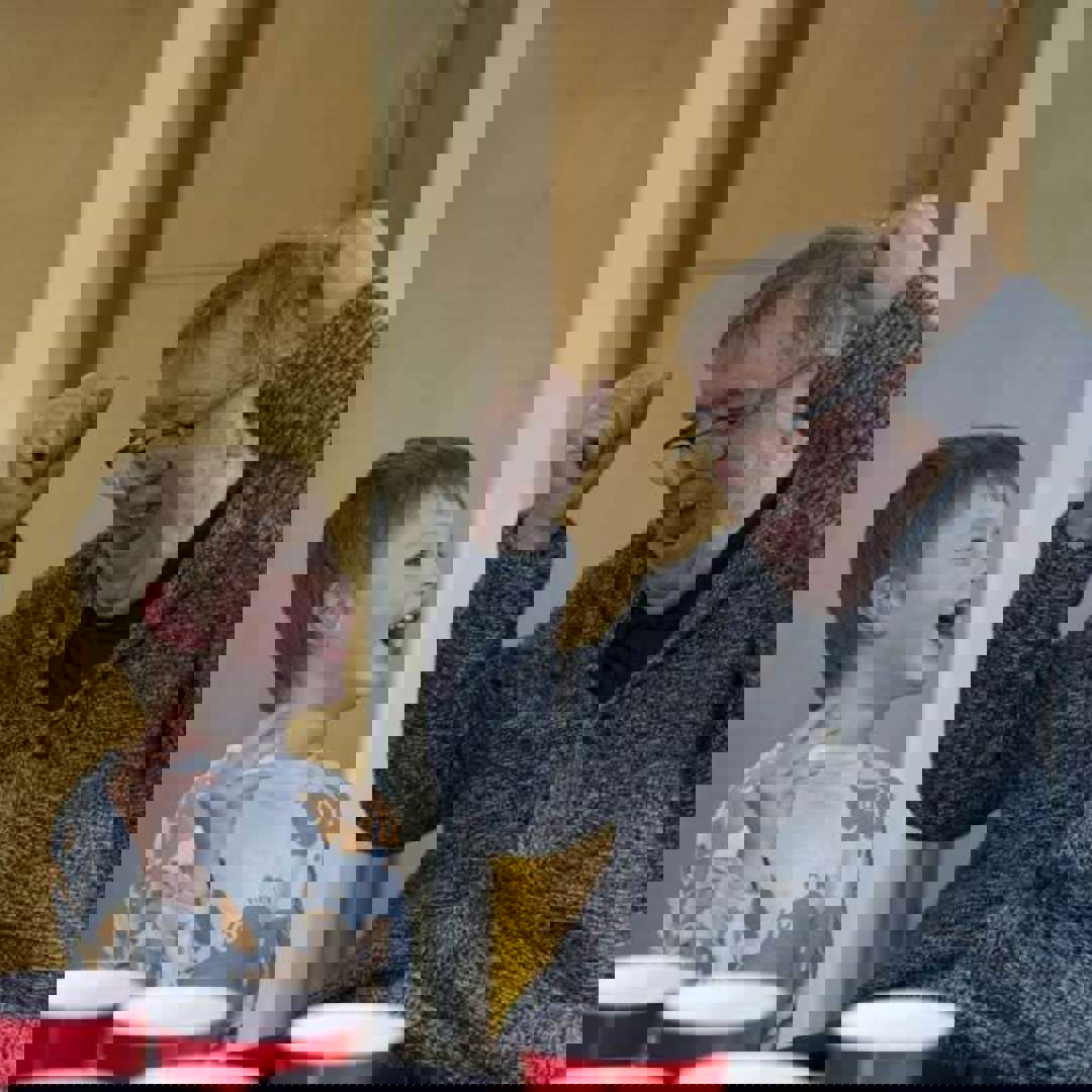 A care home resident smiles and cheers while playing a ball and cup game with a visiting nursery child