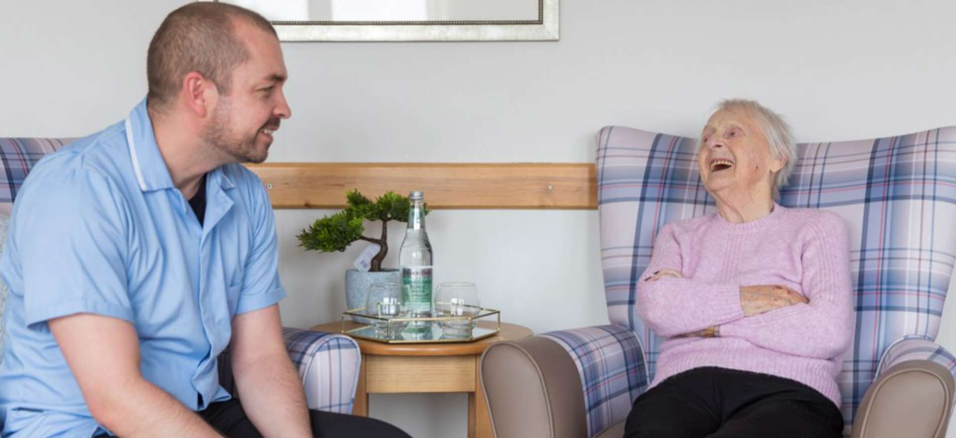 A staff member and resident sit opposite each other enjoying a conversation in a communal lounge 