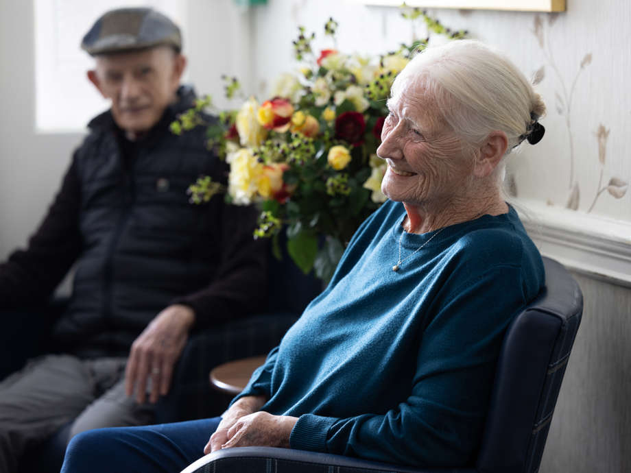 Two residents smile and laugh as they sit in the homes communal area