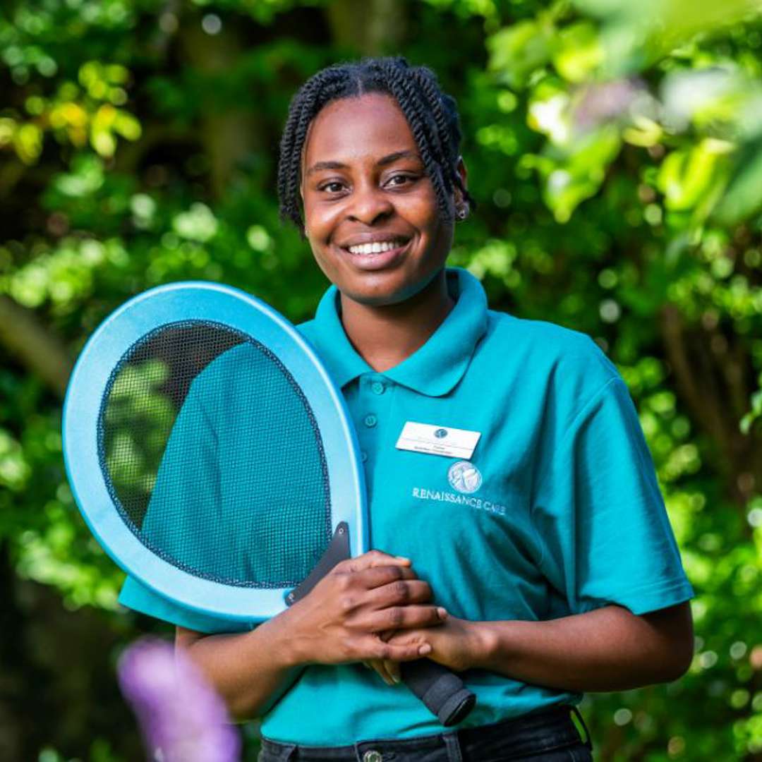 Care home staff member promotes an active lifestyle, holding a tennis racket while in uniform. 