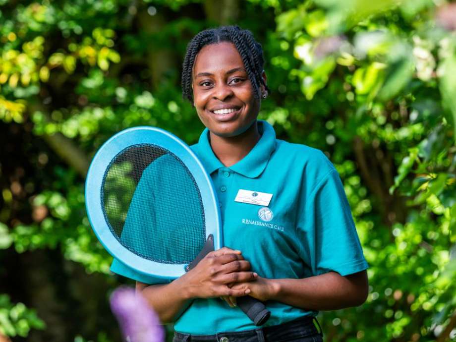 Care home staff member promotes an active lifestyle, holding a tennis racket while in uniform. 