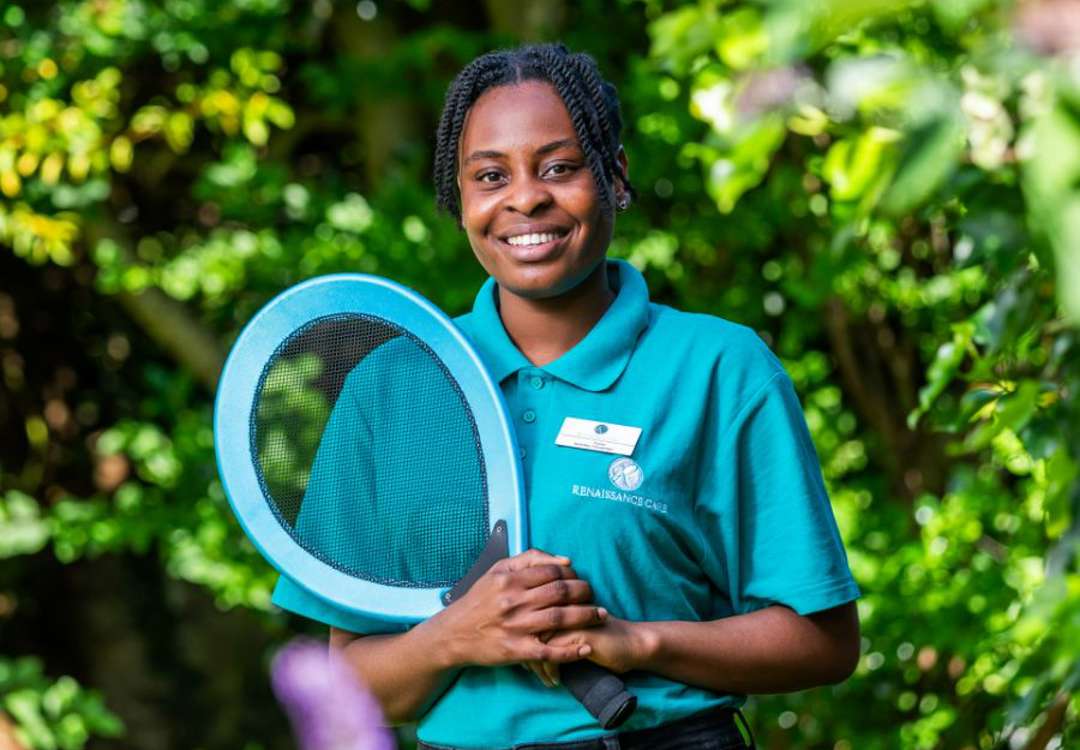 Care home staff member promotes an active lifestyle, holding a tennis racket while in uniform. 