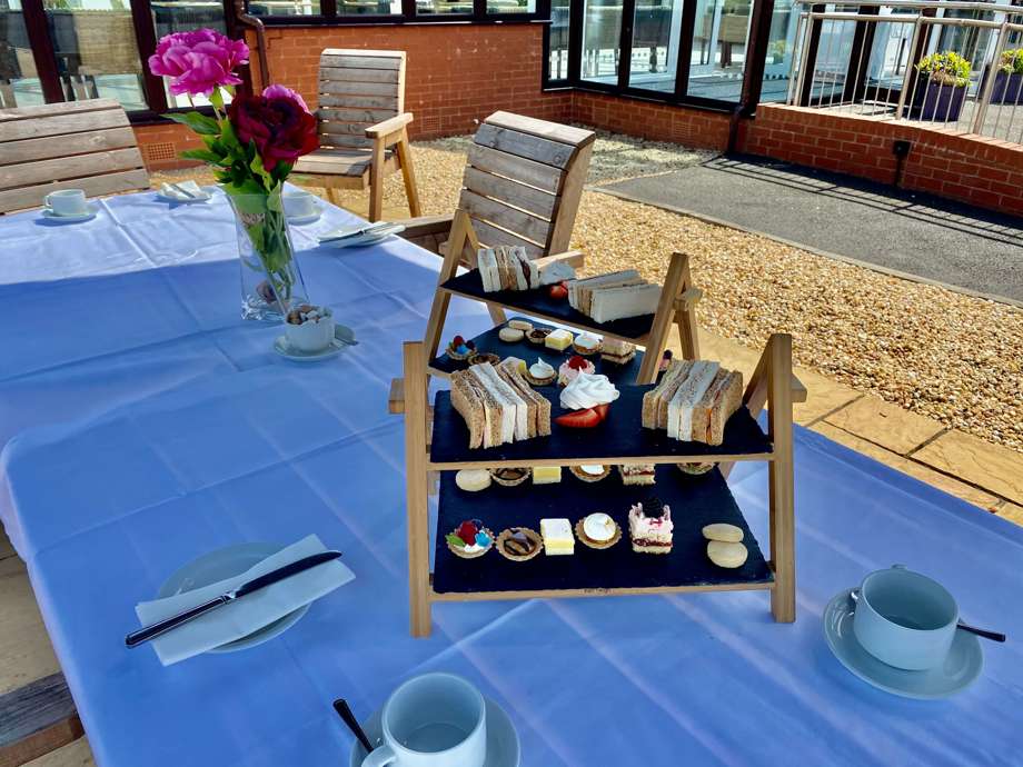 Afternoon Tea Set Up Outdoors : A table and tablecloth setup with a tray of baked goods and sandwiches