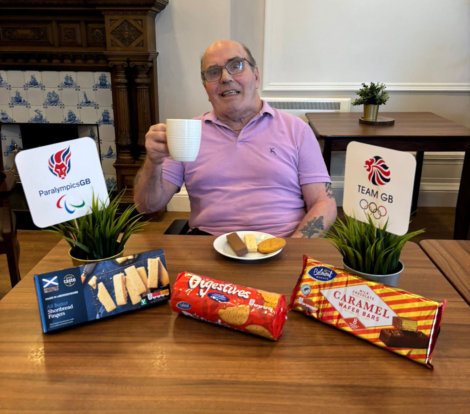 Care Home resident Ricky Tawse sits behind a table of biscuits holding up a cup of tea in search of britains most dunkable biscuit