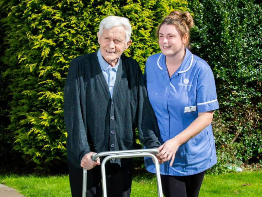 Resident enjoys the fresh air in the care home garden with the support of a care assistant and a walking aid