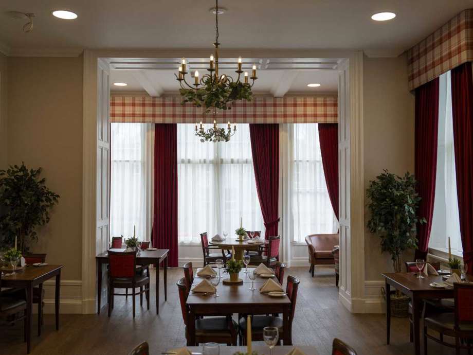 Grand dining room featuring multiple tables and chairs. Large windows with flowing red curtains bathe the space in natural light.