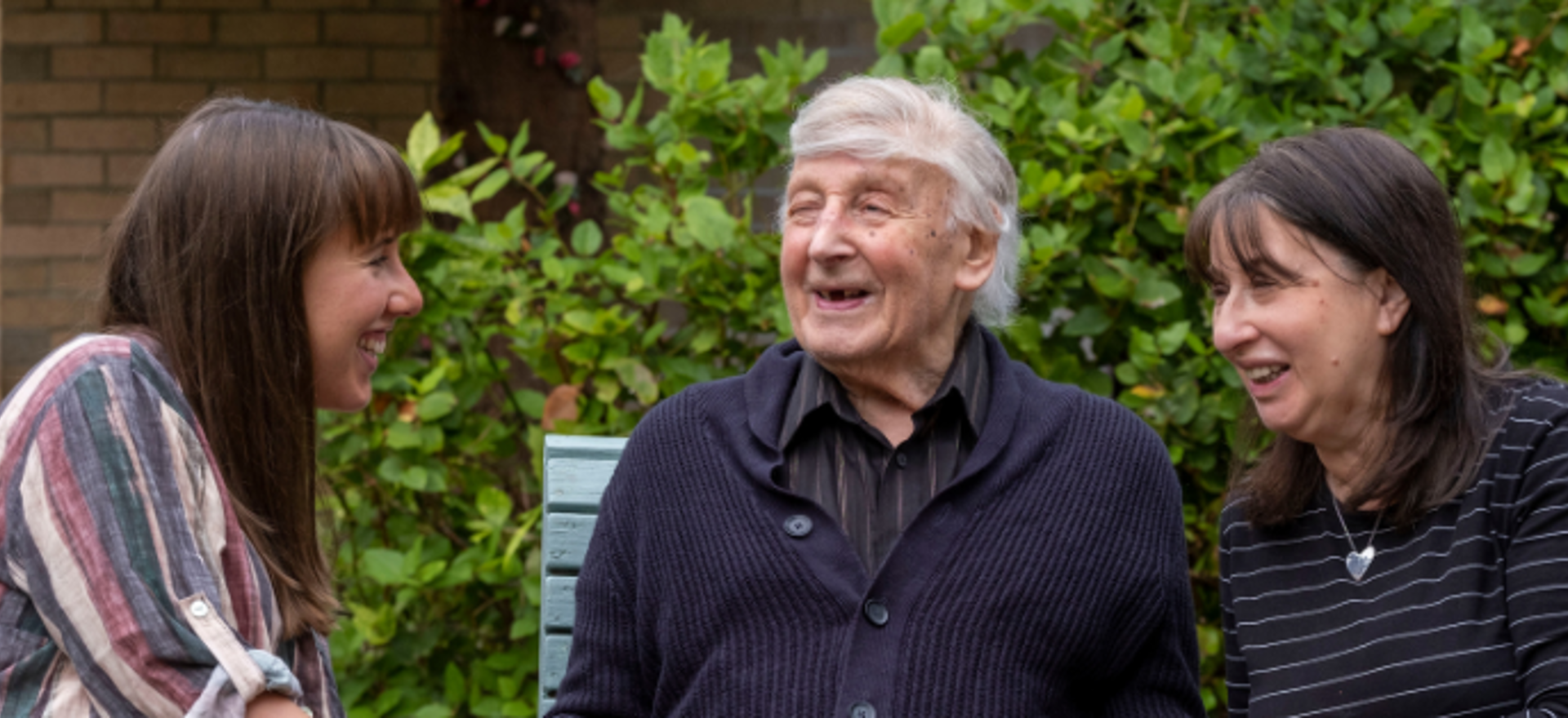 3 generations of a family are sitting in the garden as the family visit their father and grandfather respectively 