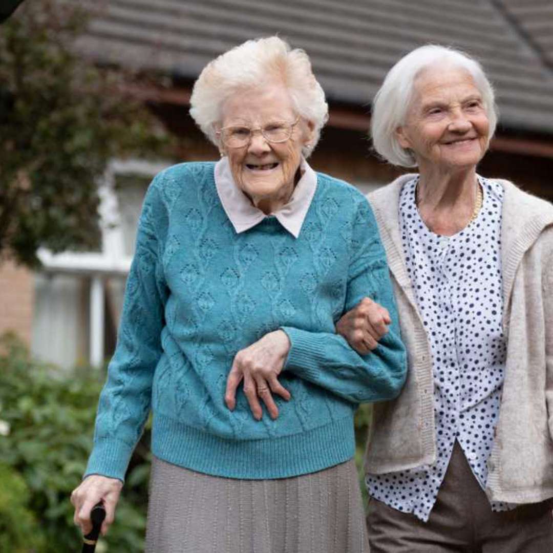 two friends linking arms walking in the care homes garden