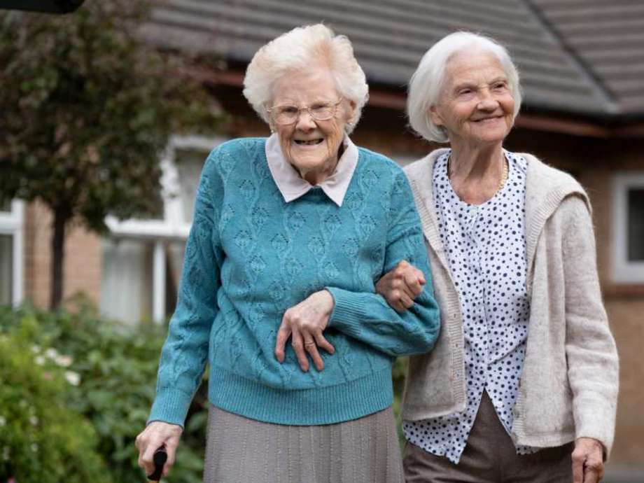 two friends linking arms walking in the care homes garden