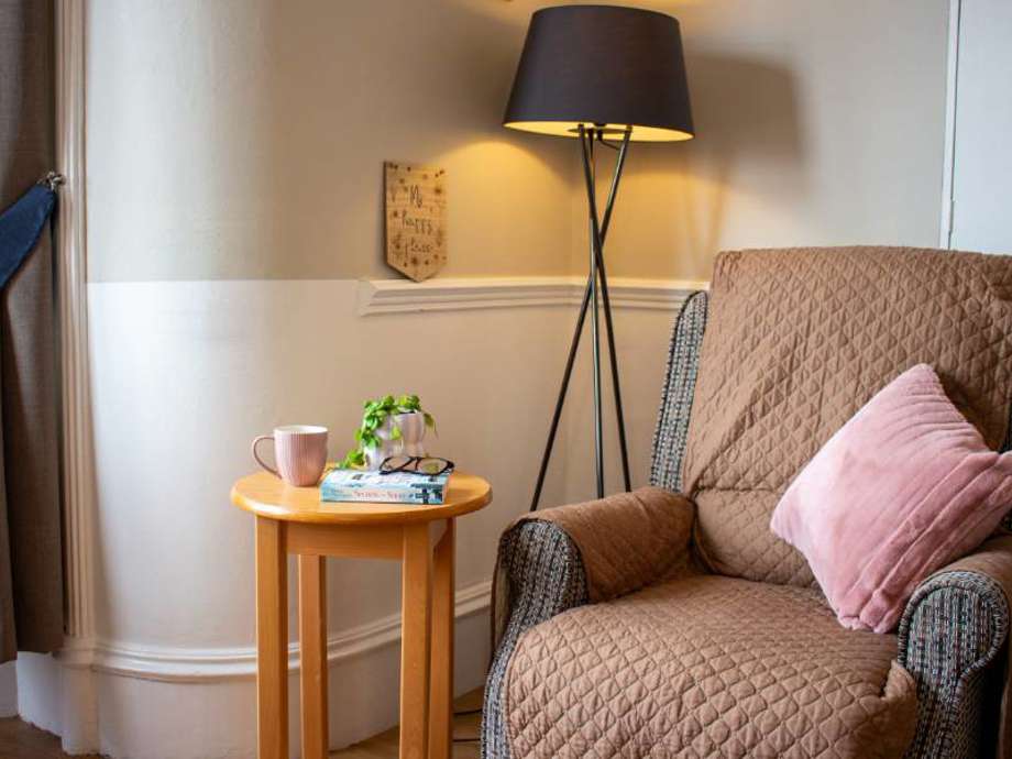 Inviting reading nook in the care home lounge. A comfortable chair with a side table and lamp creates a cosy atmosphere perfect for curling up with a book.