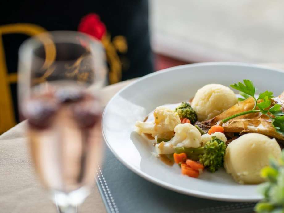 a prosecco glass with fresh fruit in the foreground with a homemade meal of vegetables, mashed potato, and steak pie in the background 