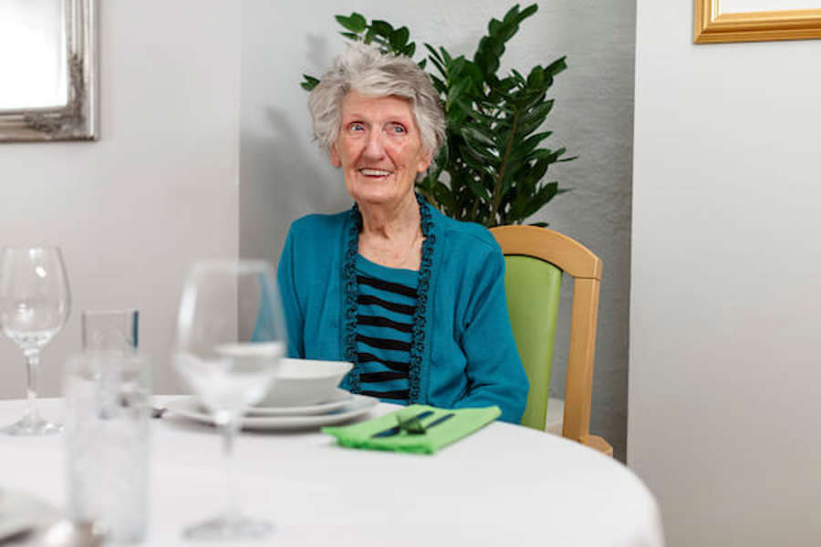 A woman is sitting on a wooden chair in the dining room, smiling