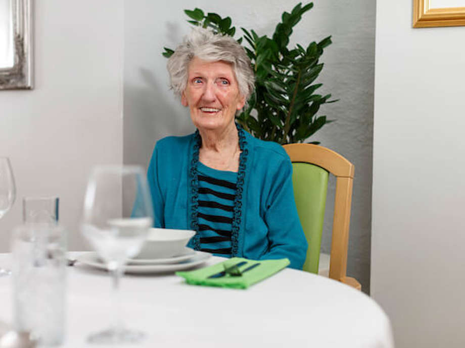 A woman is sitting on a wooden chair in the dining room, smiling