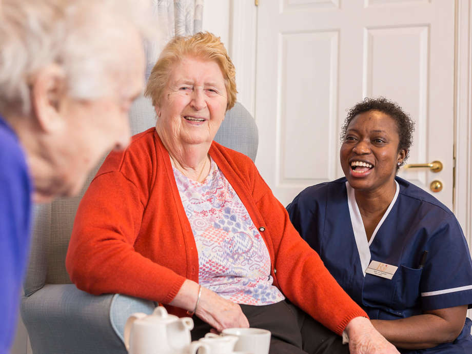 Residents enjoying a cup of tea and conversation with a staff member in the bright communal lounge.