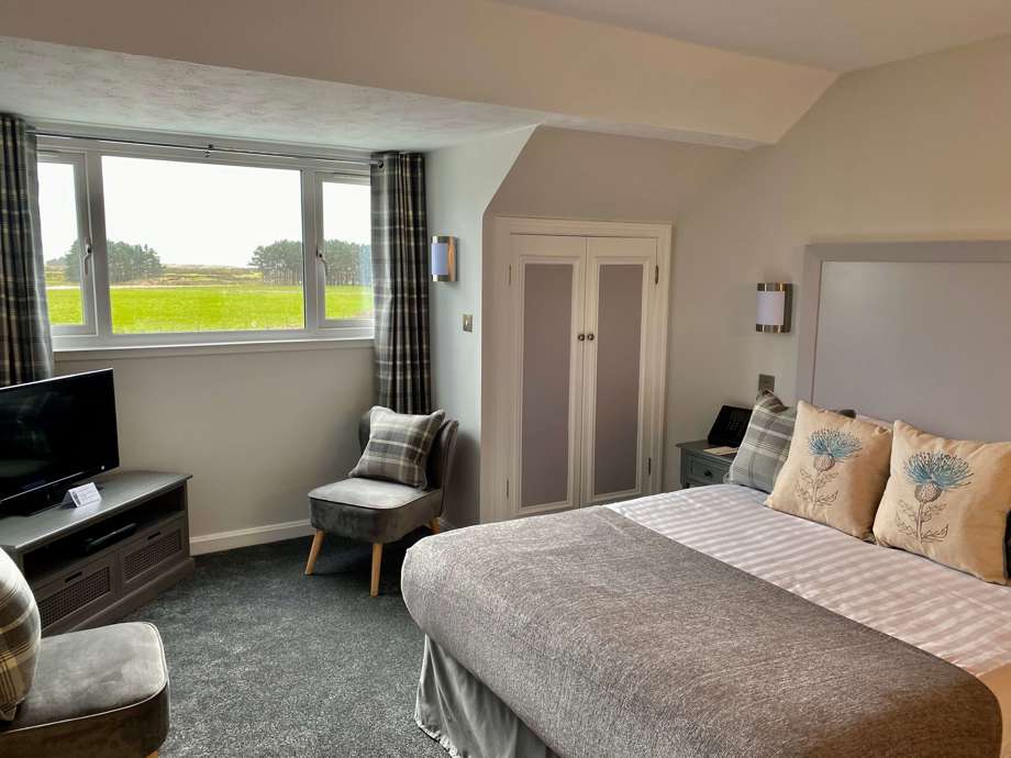 Malin Court Respite Room : A bedroom set up with bed, chair, TV unit, and window looking out into the garden 