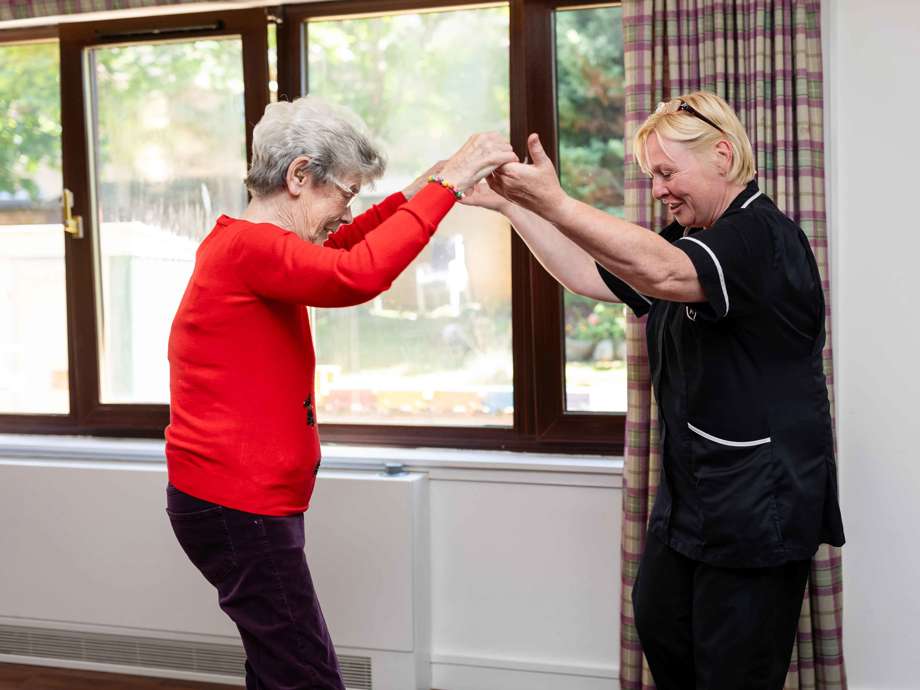 A staff member and resident enthusiastically dance together, with their arms in the air 