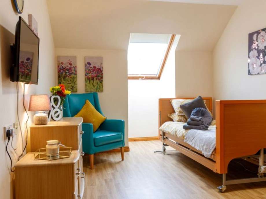 A bedroom set up with wooden furniture, brightly coloured armchair, and various artworks making it look cosy and inviting